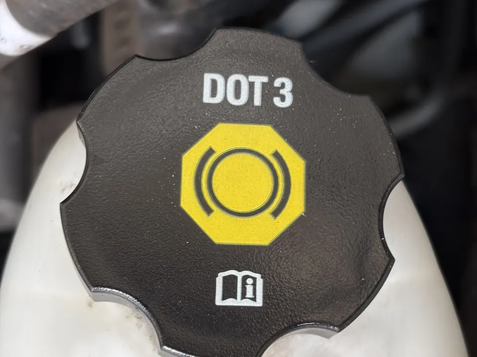 Brake fluid reservoir cap marked DOT 3 with a yellow brake symbol