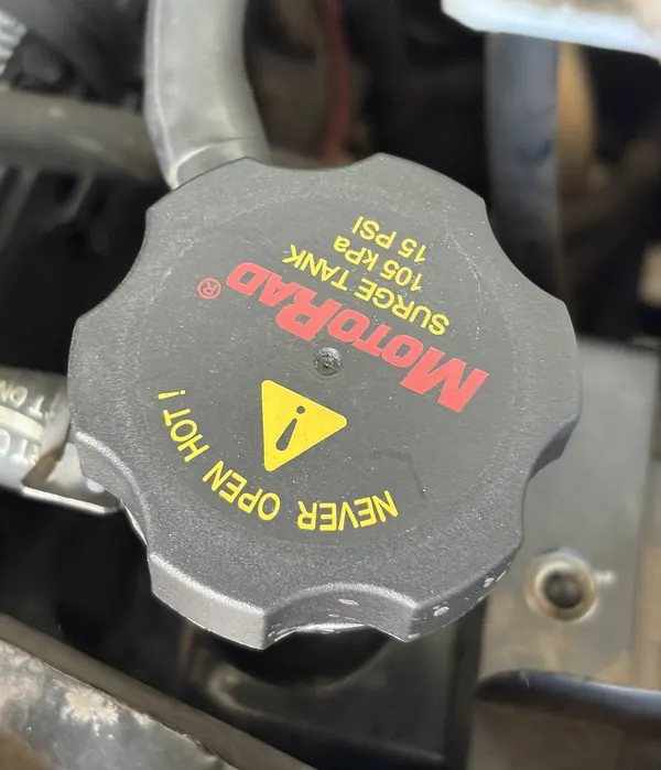 A coolant pressure cap labeled NEVER OPEN HOT