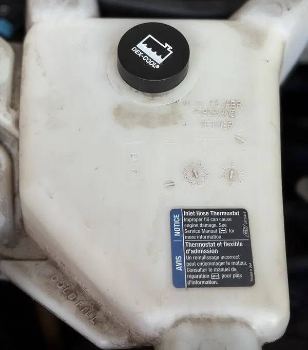 A white coolant tank with a black cap and a COLD FILL mark on its side
