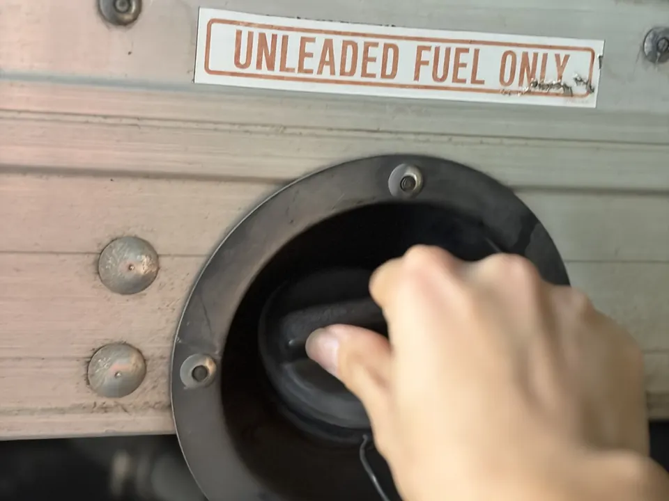 A hand tightening the fuel cap under an Unleaded Fuel Only sticker